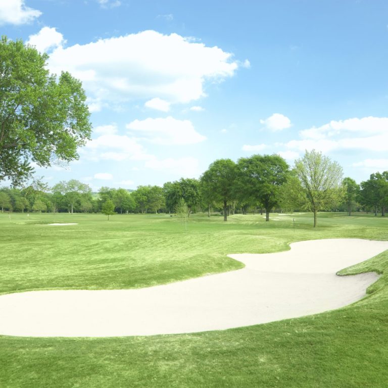 Grünes Golfplatzgelände mit einer Sandbunker und blauen Himmel.