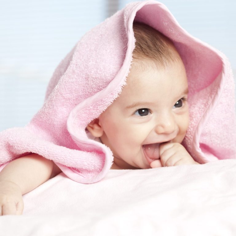 Ein lächelndes Baby mit einer rosa Decke beißt auf den Daumen.